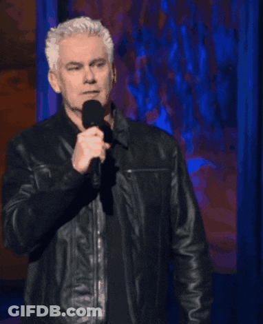 A Man In A Leather Jacket Stands In Front Of A Microphone With The Words Get A Dictionary Above Him GIF