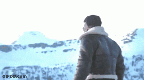 A Man In A Leather Jacket Stands In Front Of A Snowy Landscape GIF