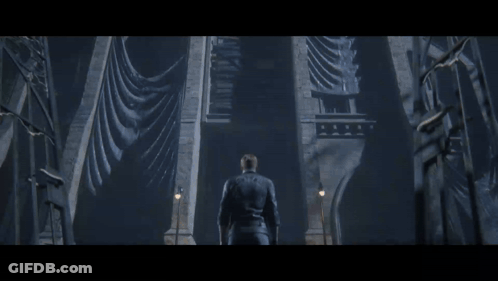 A Man In A Leather Jacket Stands In Front Of A Very Tall Building GIF