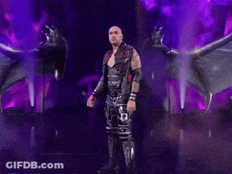 A Man In A Leather Vest With The Letter R On It Stands On A Stage GIF