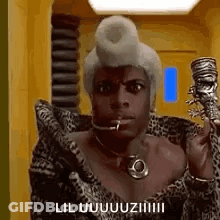 A Man In A Leopard Print Coat Is Holding A Cane In His Hand And Talking On A Cell Phone . GIF