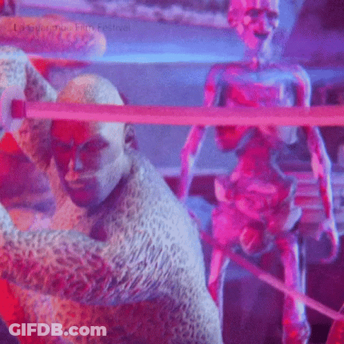 A Man In A Leopard Print Costume Is Standing Next To A Statue Of A Man With A Sword . GIF