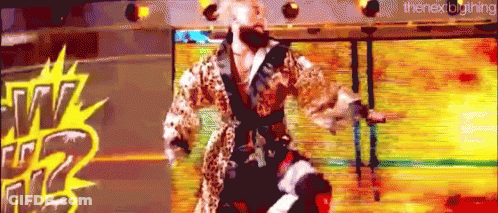A Man In A Leopard Print Robe Is Standing On A Stage In Front Of A Large Screen . GIF