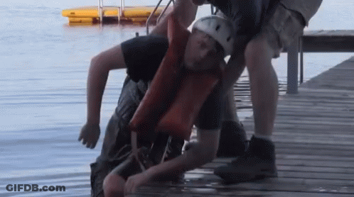 A Man In A Life Jacket Is Being Lifted Out Of The Water GIF