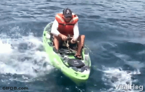 A Man In A Life Jacket Is Riding A Green Kayak On A Lake GIF