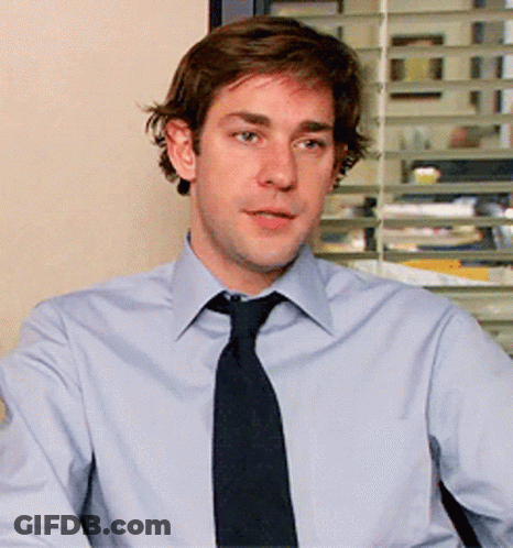 A Man In A Light Blue Shirt And Black Tie Looks At The Camera GIF