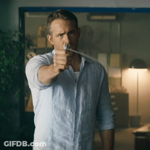 A Man In A Light Blue Shirt Is Pointing A Gun GIF