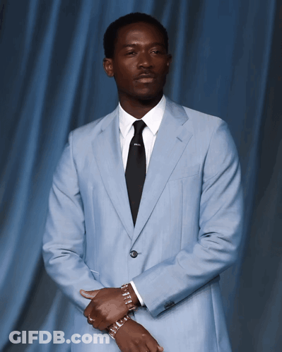 A Man In A Light Blue Suit And Black Tie Has A Bracelet On His Wrist GIF