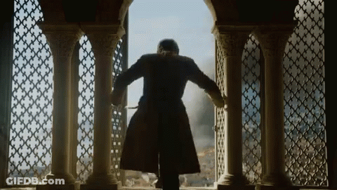 A Man In A Long Coat Is Standing In Front Of A Window With Columns . GIF