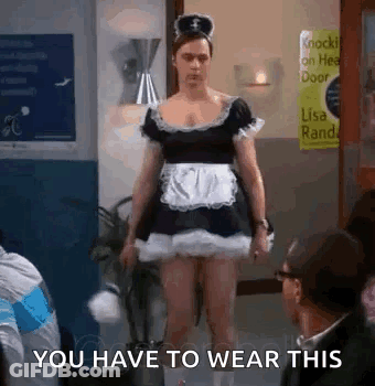 A Man In A Maid Costume Is Standing In A Room With People . GIF