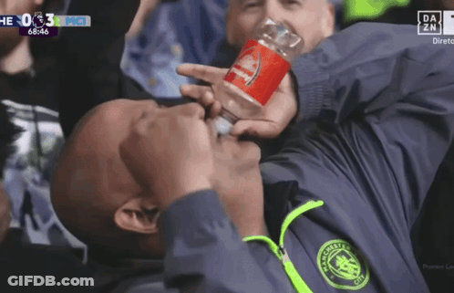 A Man In A Manchester City Jacket Drinks From A Bottle GIF