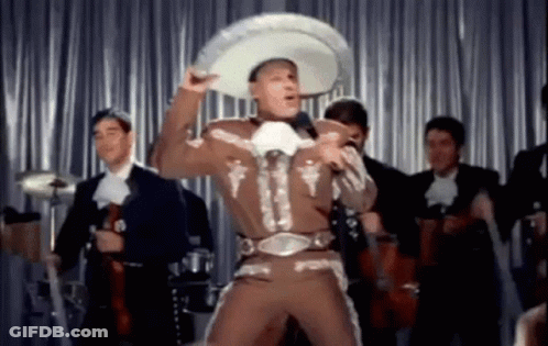 A Man In A Mariachi Outfit And Sombrero Is Singing Into A Microphone . GIF