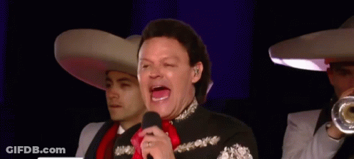 A Man In A Mariachi Outfit Is Singing Into A Microphone While Two Men Play Trumpets In The Background GIF