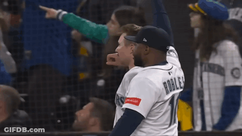 A Man In A Mariners Jersey Stands With Another Man GIF