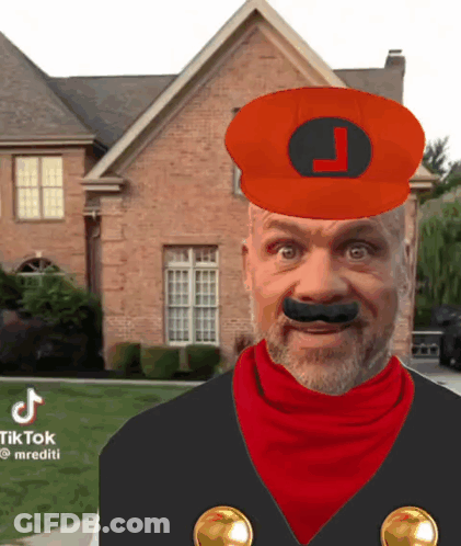 A Man In A Mario Costume Is Standing In Front Of A Brick House With A Red Hat And Mustache . GIF