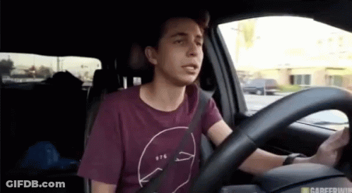 A Man In A Maroon Shirt Is Driving A Car With A Seat Belt On . GIF