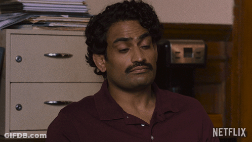 A Man In A Maroon Shirt Is Sitting In Front Of A Netflix Logo GIF