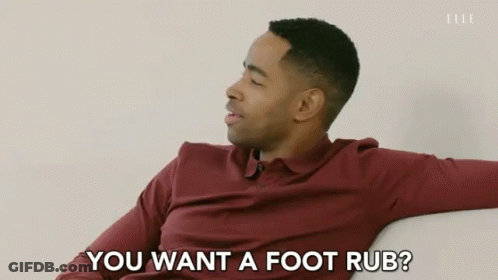 A Man In A Maroon Shirt Is Sitting On A Couch And Says " You Want A Foot Rub " GIF