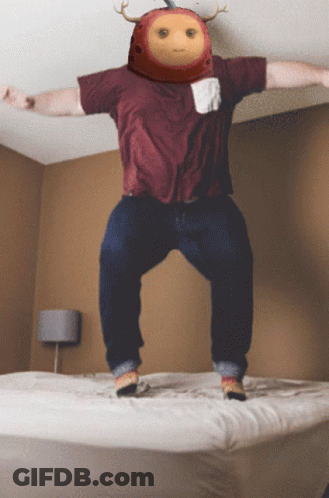 A Man In A Maroon Shirt Jumps On A Bed GIF
