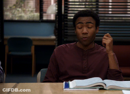 A Man In A Maroon Shirt Sits At A Desk With A Book GIF