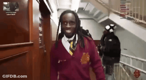 A Man In A Maroon Sweater And Tie Is Walking Down Stairs GIF