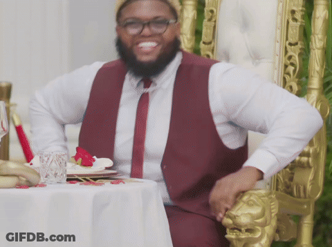 A Man In A Maroon Vest And Tie Is Sitting In A Chair GIF