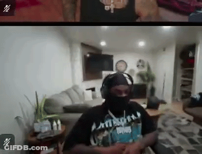 A Man In A Mask And Headphones Is Sitting In A Living Room . GIF