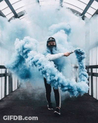 A Man In A Mask Holds A Blue Smoke Bomb In His Hand GIF