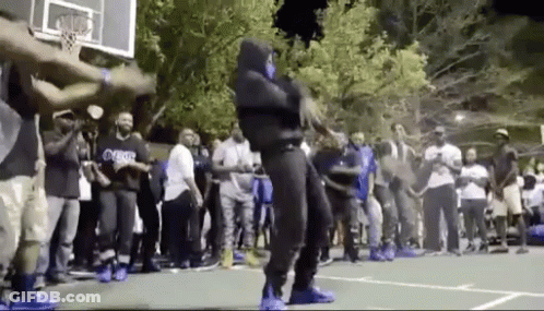 A Man In A Mask Is Dancing On A Basketball Court In Front Of A Crowd Of People . GIF