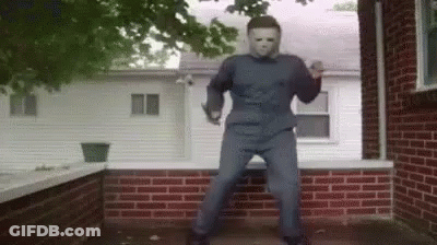 A Man In A Mask Is Dancing On A Porch In Front Of A Brick House . GIF