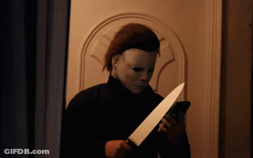 A Man In A Mask Is Holding A Knife And Looking At His Phone GIF