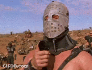 A Man In A Mask Is Holding A Microphone In A Desert . GIF