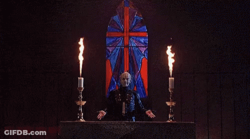 A Man In A Mask Is Holding Two Candles In Front Of A Burning Building . GIF