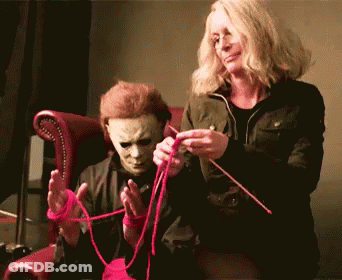 A Man In A Mask Is Sitting Next To A Woman Who Is Knitting GIF