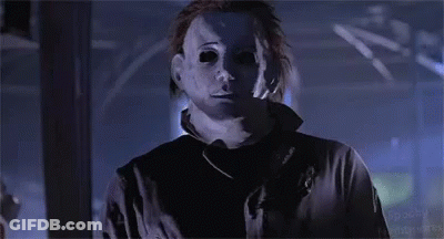 A Man In A Mask Is Standing In A Dark Room And Looking At The Camera . GIF
