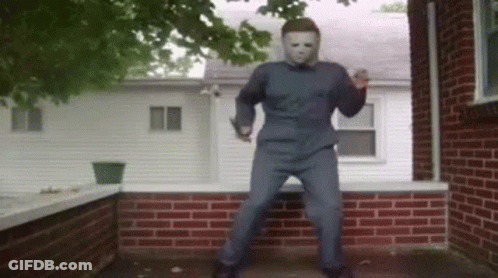 A Man In A Mask Is Standing In Front Of A Brick Building . GIF