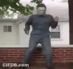 A Man In A Mask Is Standing In Front Of A Brick Building . GIF