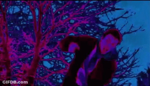 A Man In A Mask Is Standing In Front Of A Tree In A Dark Room . GIF