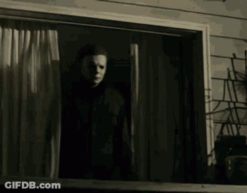 A Man In A Mask Is Standing In Front Of A Window In A Dark Room . GIF