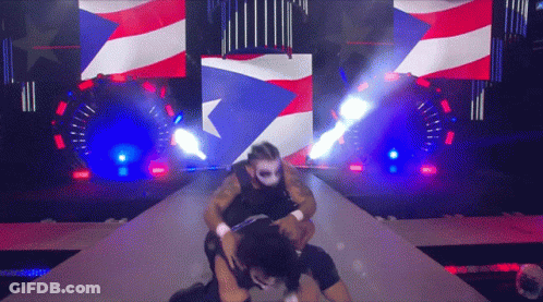A Man In A Mask Is Wrestling Another Man In Front Of An American Flag GIF