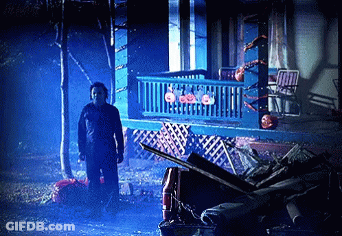 A Man In A Mask Stands In Front Of A House With Pumpkins On It GIF