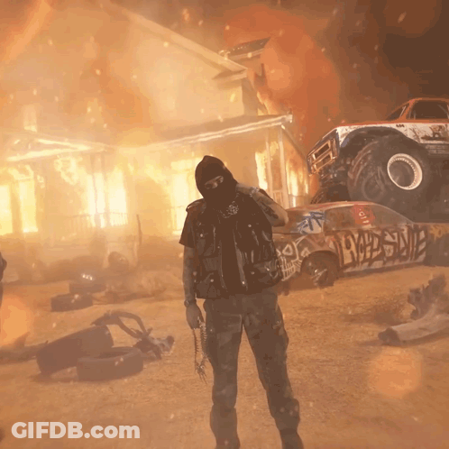 A Man In A Mask Stands In Front Of A Monster Truck And A Burning House With Graffiti On It GIF