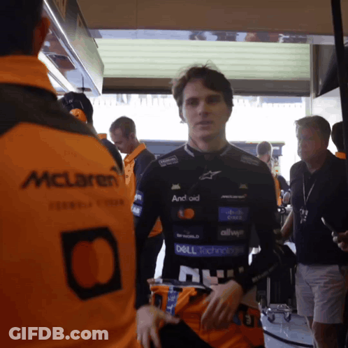 A Man In A Mclaren Jacket Is Standing In A Garage GIF