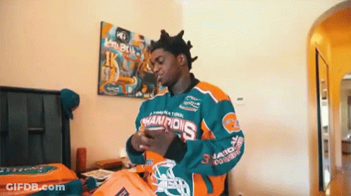 A Man In A Miami Dolphins Jersey Is Standing In A Bedroom Holding A Bag . GIF