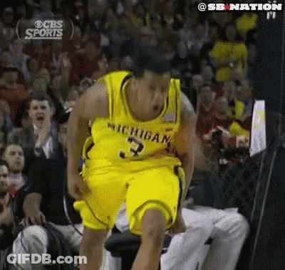 A Man In A Michigan Jersey Is Jumping In The Air In Front Of A Crowd GIF