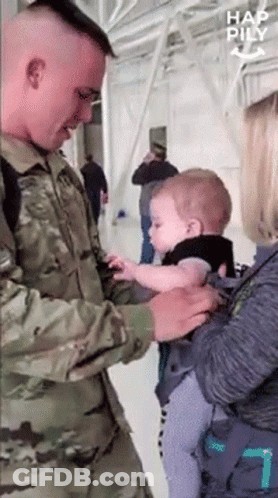 A Man In A Military Uniform Holds A Baby In A Carrier GIF