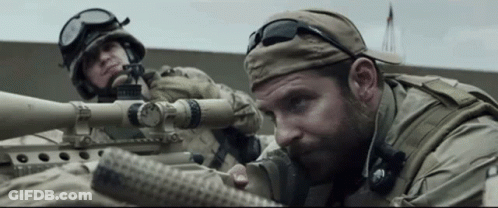 A Man In A Military Uniform Is Aiming A Sniper Rifle . GIF