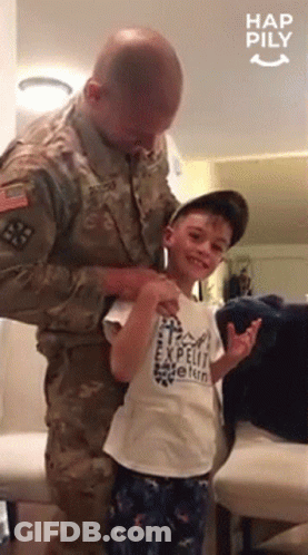 A Man In A Military Uniform Is Putting A Shirt On A Young Boy Who Is Wearing A Shirt That Says Expedit Vetern GIF