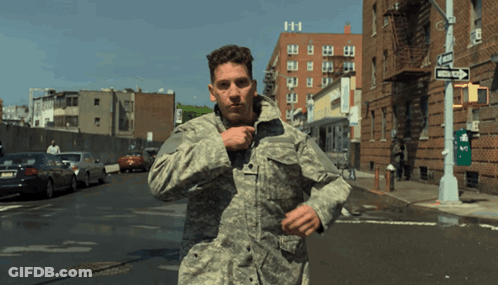 A Man In A Military Uniform Is Running Down A Street With A One Way Sign In The Background GIF
