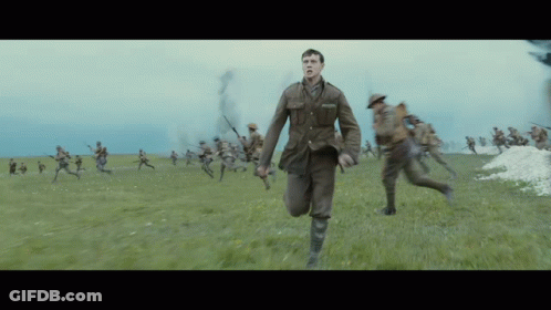 A Man In A Military Uniform Is Running In A Field With Soldiers Behind Him GIF